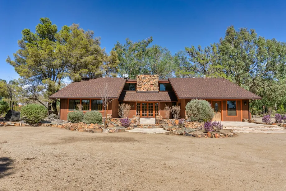 Single-storey ranch house with a low hipped roof and stone chimney among trees