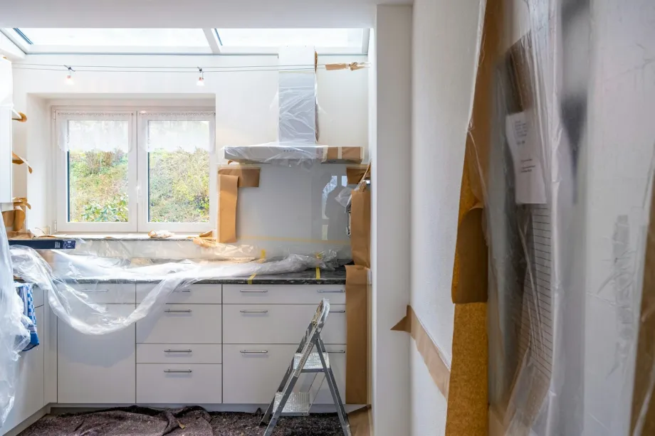 Kitchen under renovation with white cabinets covered in plastic and brown paper