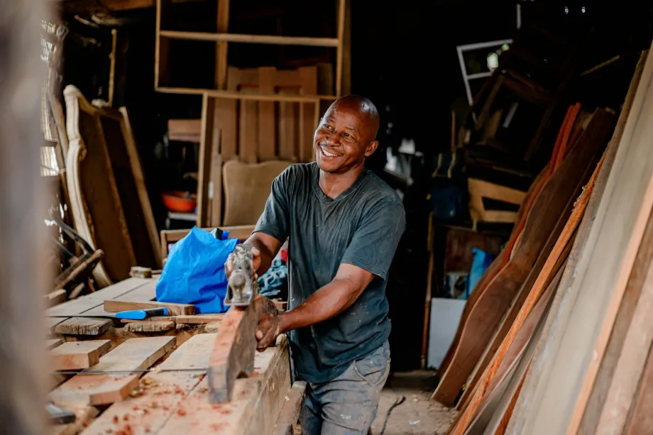 Carpenter smiling as he works on a piece of wood in a workshop